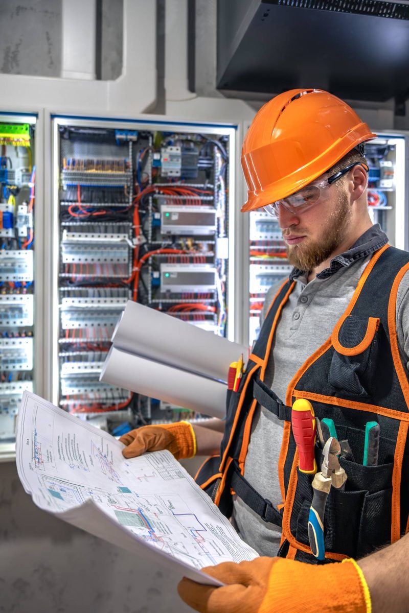 Male electrician working in electrical panel. Male electrician in uniform. High quality photo. Male construction worker in helmet and safety glasses.